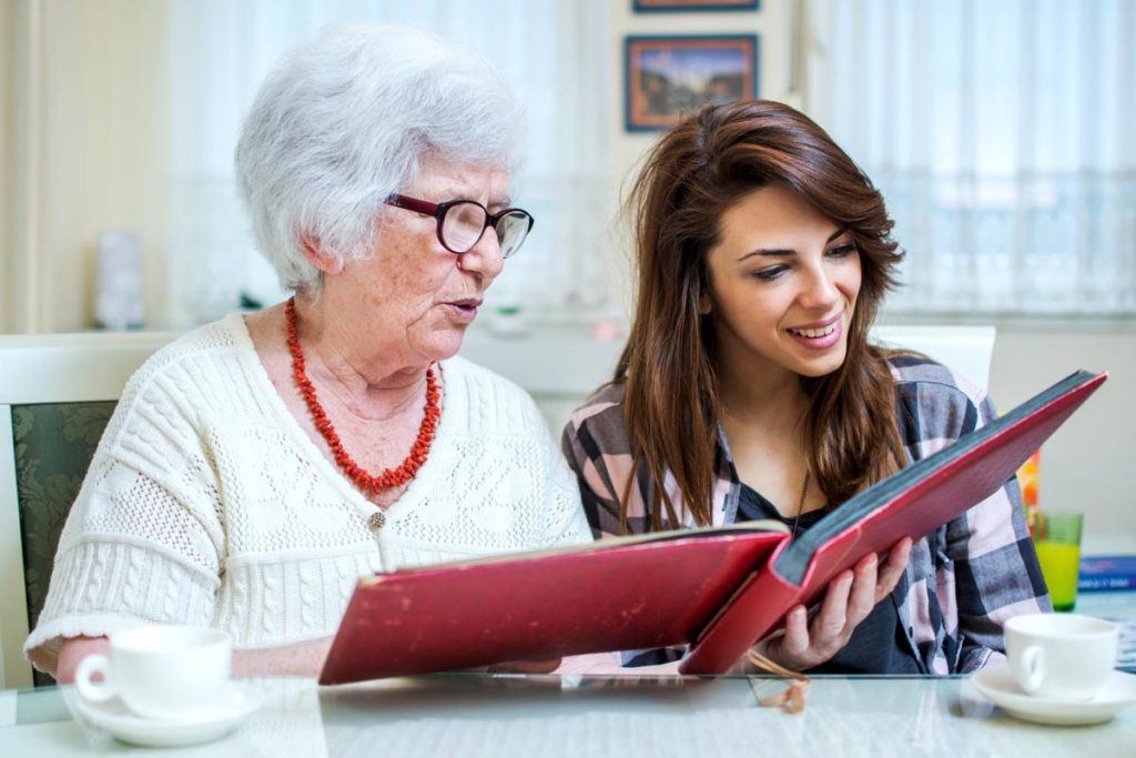 daughter and senior woman looking at photo album talking about moving a parent into senior memory care
