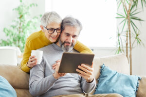one of many married couples in senior living embrace while looking at a tablet