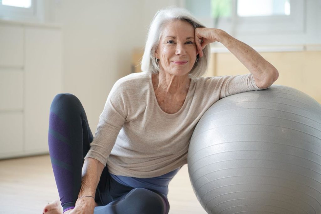 senior woman sitting with a medicine ball and who has added exercise to her senior routines