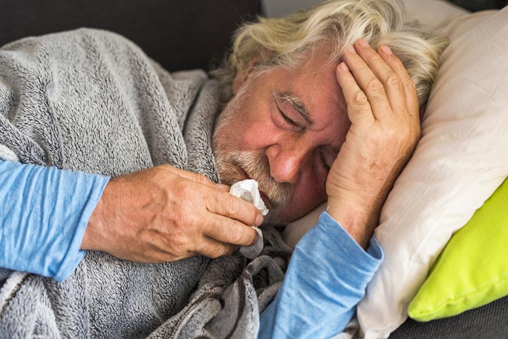 an older adult lays in bed with a cold and probably experiencing pneumonia in seniors
