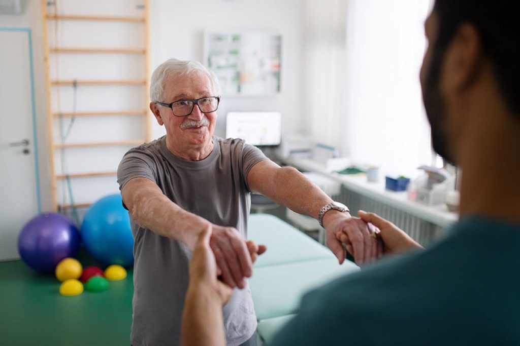 a senior male participates in physical therapy for seniors as a male nurse helps him with his mobility
