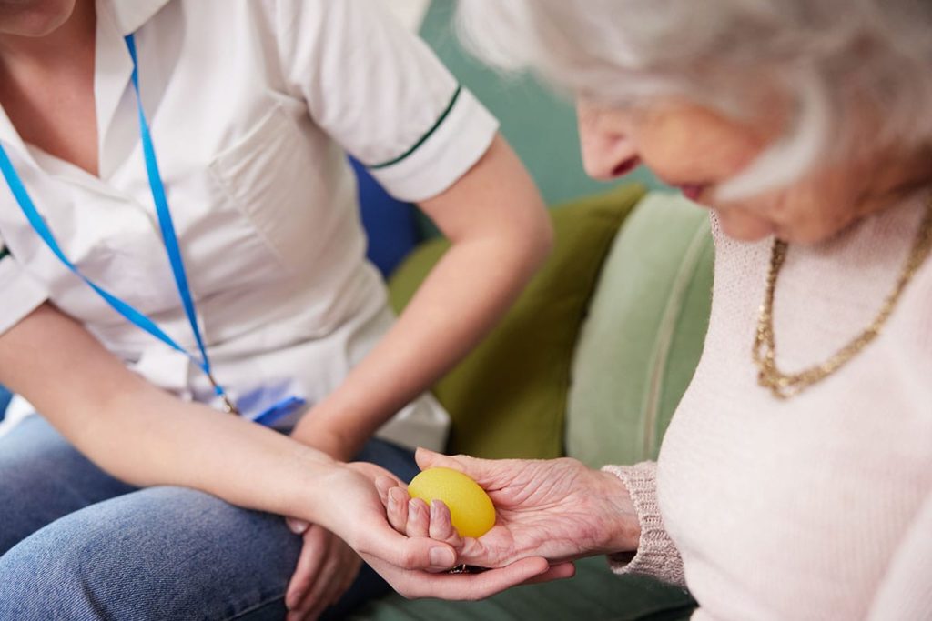 a nurse helps a senior woman hold a ball in her hand as one of the exercises for occupational therapy for seniors