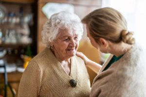 an adult woman pats a senior woman on her shoulder while expressing some tips for caring for someone with dementia to her family