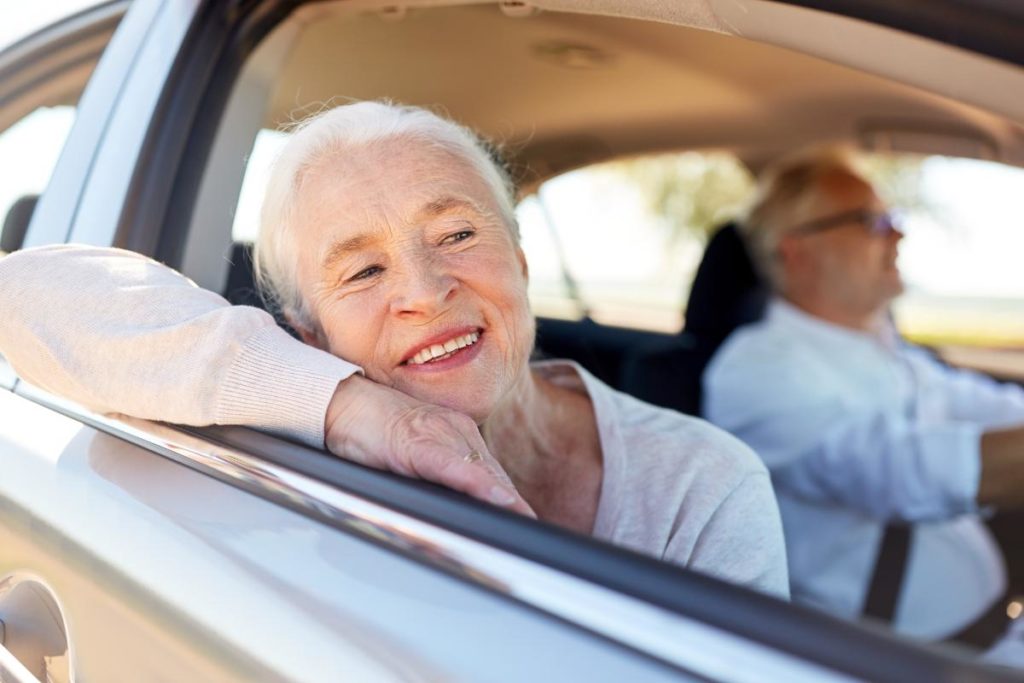 a senior woman sticks her head out the passenger side of a car after while her senior husband drives wondering when should seniors should stop driving