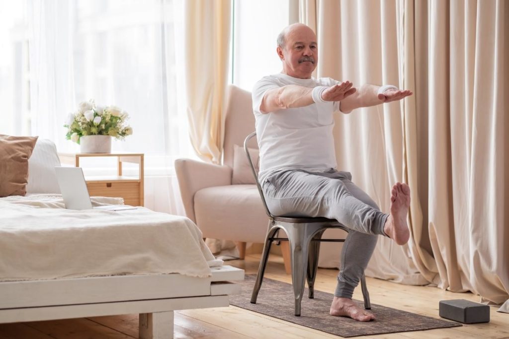 a senior male is practicing chair yoga for seniors in his home