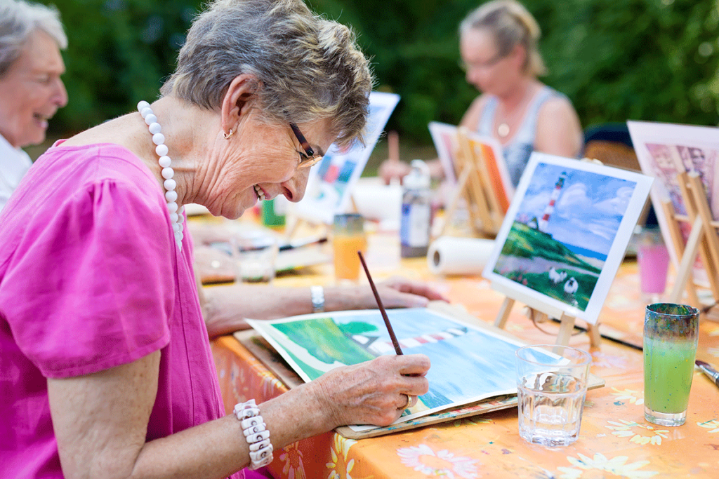seniors join in on a fun activity together painting outside in their retirement community