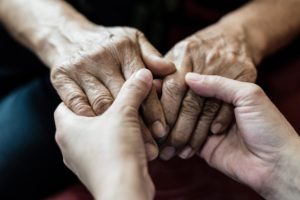 a person holds the hands of someone going through the stages of alzheimer's