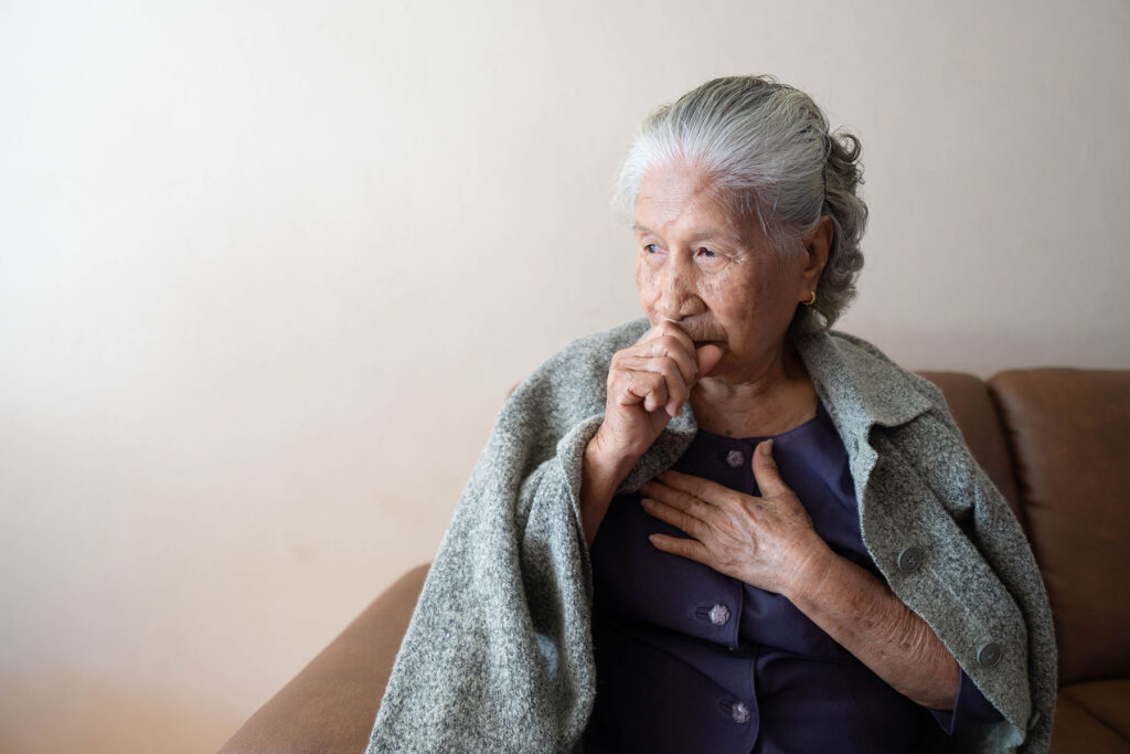 a person holds their chest while wrapped in a blanket as they exhibit signs of Pneumonia in seniors