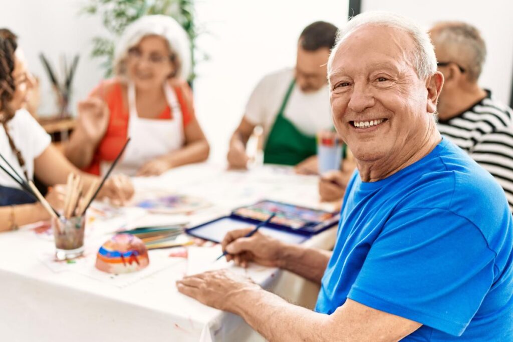 a senior smiles as he does art in Recreational Programs in for those in their Retirement Years