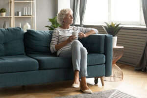 A woman enjoys staying independent in retirement by aging in place. She relaxes on her couch while drinking a cup of coffee.