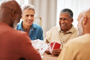 Some men laugh together as they play cards at a table. They are reaping the benefits of senior social interaction.