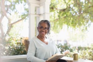 A woman is smiling while she reads a book and engages in senior habits for memory retention.