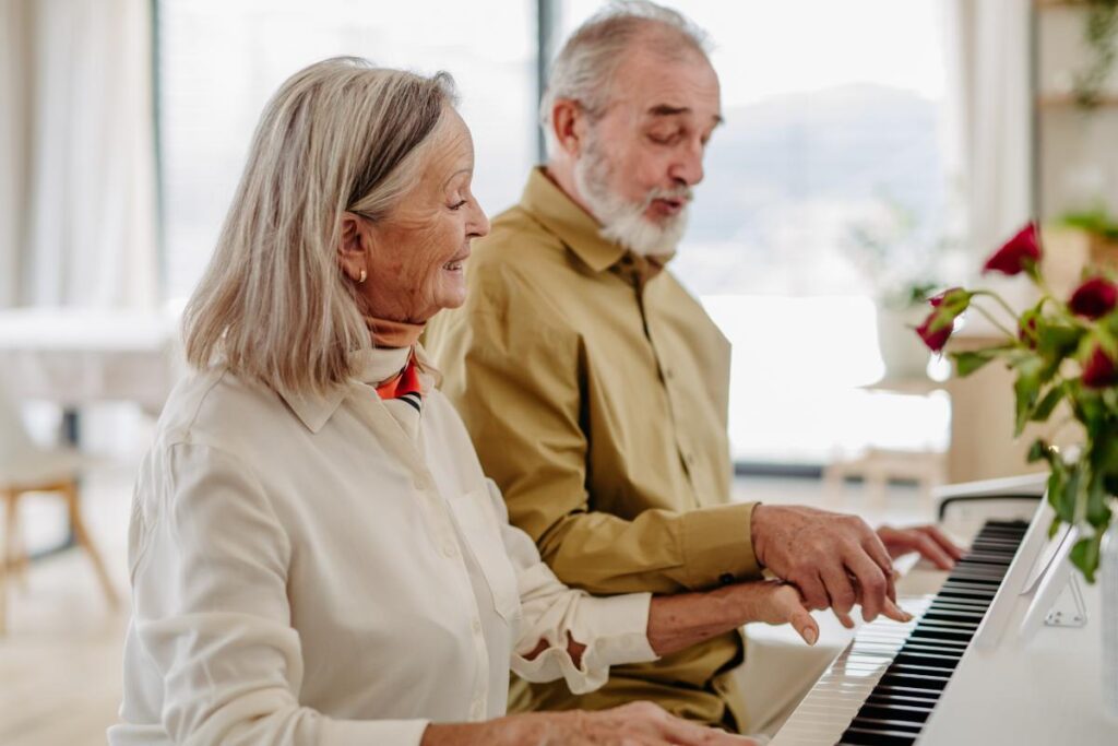 A senior man teaches piano to a senior woman, they are both benefiting from volunteering in retirement.