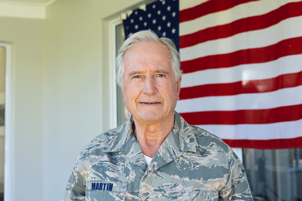 A senior man in uniform and standing in front of a US flag is enjoying senior living for veterans.