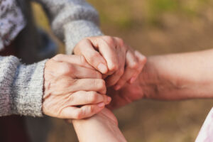 A senior adult is holding hands with a counselor. They are receiving comfort as they manage chronic health conditions in senior living.