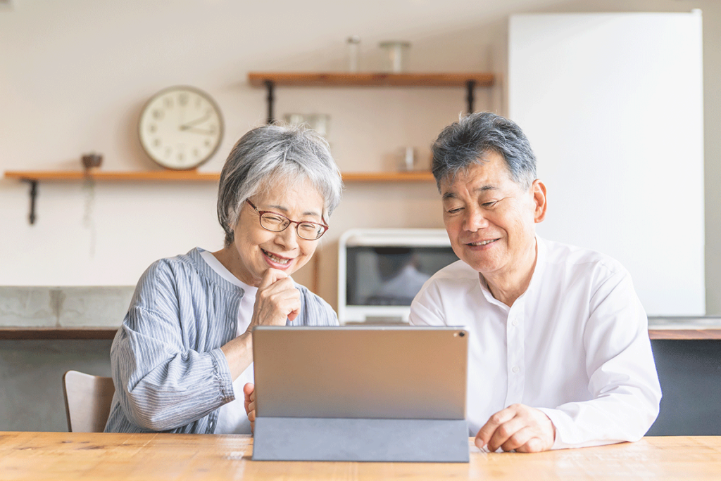 A senior couple sit at a table and enjoy a senior living educational program via their tablet. This is part of their lifelong learning.