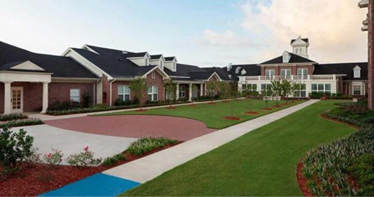 A modern brick building with white trim, landscaped lawns, paths, and a central courtyard under a partly cloudy sky.